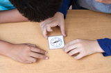 The picture shows two children looking at a compass box together. They place their hands on the table and carefully focus on the compass needle while exploring the cardinal directions.