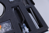 The image shows an assorted toolbox with various experimental supplies, including glass tubes and a round, reflective container. The supplies are neatly arranged in a foam-padded compartment, indicating careful presentation.