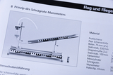 The picture shows an experimental setup for an inclined tube manometer, consisting of an inclined plate, a measuring container and connecting tubes. It is a guide for carrying out an experiment in the field of physics and fluid dynamics.