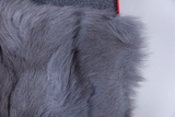 The image shows a piece of grey fur fabric, the soft and fluffy structure of which is clearly visible. In the background, a dark, structured surface can be seen, which provides a contrasting frame for the fur.