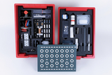 The picture shows a red storage box equipped with various experimental materials, including electrical components, chemical substances and tools. In the middle of the set is a circuit board with several contacts that can be used for experiments.