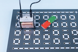 The picture shows an experimental arrangement with a coil attached to a grid of holes while a red-green rotor blade rotates. The setup is designed for physics experiments to demonstrate electromagnetic effects.
