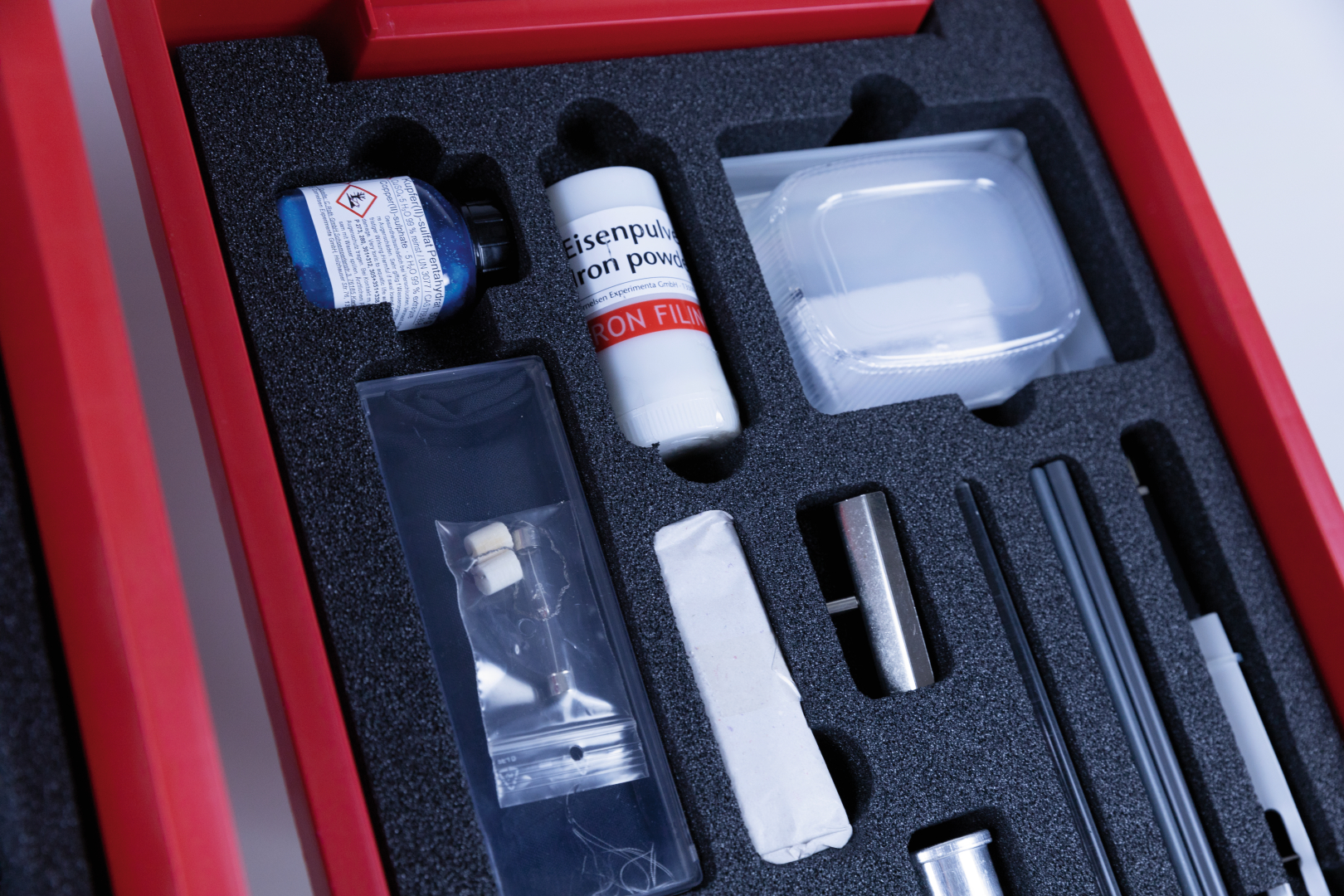 The picture shows an experiment kit with various components, including iron powder, liquids in containers and other utensils arranged on a foam tray. This kit is probably used to conduct chemical or physical experiments in educational settings.