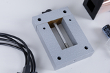 The image shows a gray, rectangular device with a central opening and a metal pin, surrounded by cables and other components. It appears to be part of an experiment kit used in education.