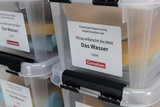 The picture shows experiment kits from the supplier Cornelsen, which contain various materials for experimenting with water. One set is labeled &quot;Virus explores the world - Water&quot; and is designed for educational purposes.