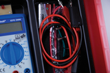 The picture shows a multimeter with various connecting cables and a 9-volt battery. This equipment is typically designed for experiments and measurements in educational settings.