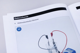 The picture shows a page from a textbook on electrochemistry describing an electrochemical element. It shows a transparent container with electrodes and cables as well as a measuring device for displaying values.