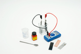 The picture shows experimental equipment consisting of a beaker with liquid, two electrodes, a multimeter for measuring electrical values, as well as various metal samples and a package with citric acid. These materials are suitable for chemical and physical experiments in education.