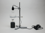 The picture shows an experimental device with a lamp holder mounted above a funnel. Below is a black container, probably used for chemical experiments or as part of a physics experiment.