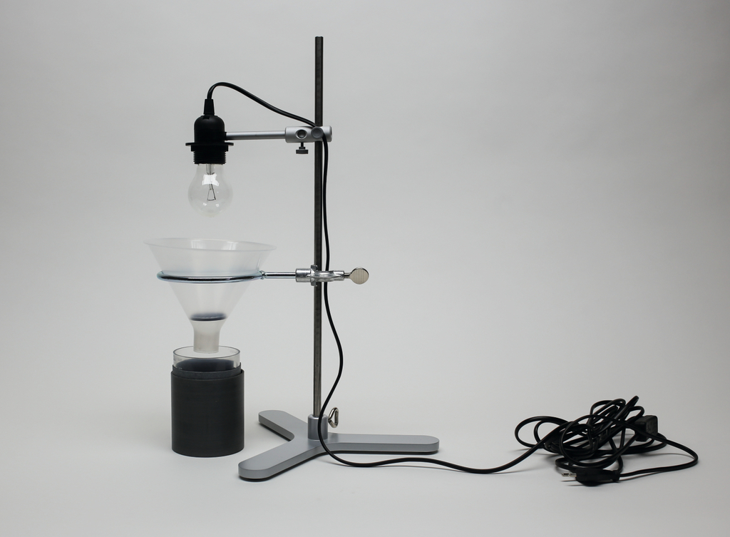 The picture shows an experimental device with a lamp holder mounted above a funnel. Below is a black container, probably used for chemical experiments or as part of a physics experiment.