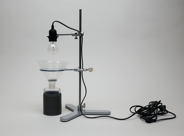 The picture shows an experimental device with a lamp holder mounted above a funnel. Below is a black container, probably used for chemical experiments or as part of a physics experiment.