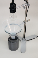 The picture shows an experimental device that consists of a holder with a light source and a transparent funnel. Underneath the funnel is a cylinder that is probably used to hold liquids or gases.