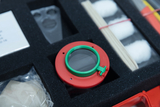 The picture shows a box with various experimental materials, including a red-green lens device and several components. The arrangement on black foam highlights the individual parts, which can be used for educational or experimental purposes.