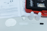 The image shows a collection of experimental materials, including test tubes, pipettes, slides, and an instruction manual related to biological experiments. The materials are organized in a red case designed for educational use.