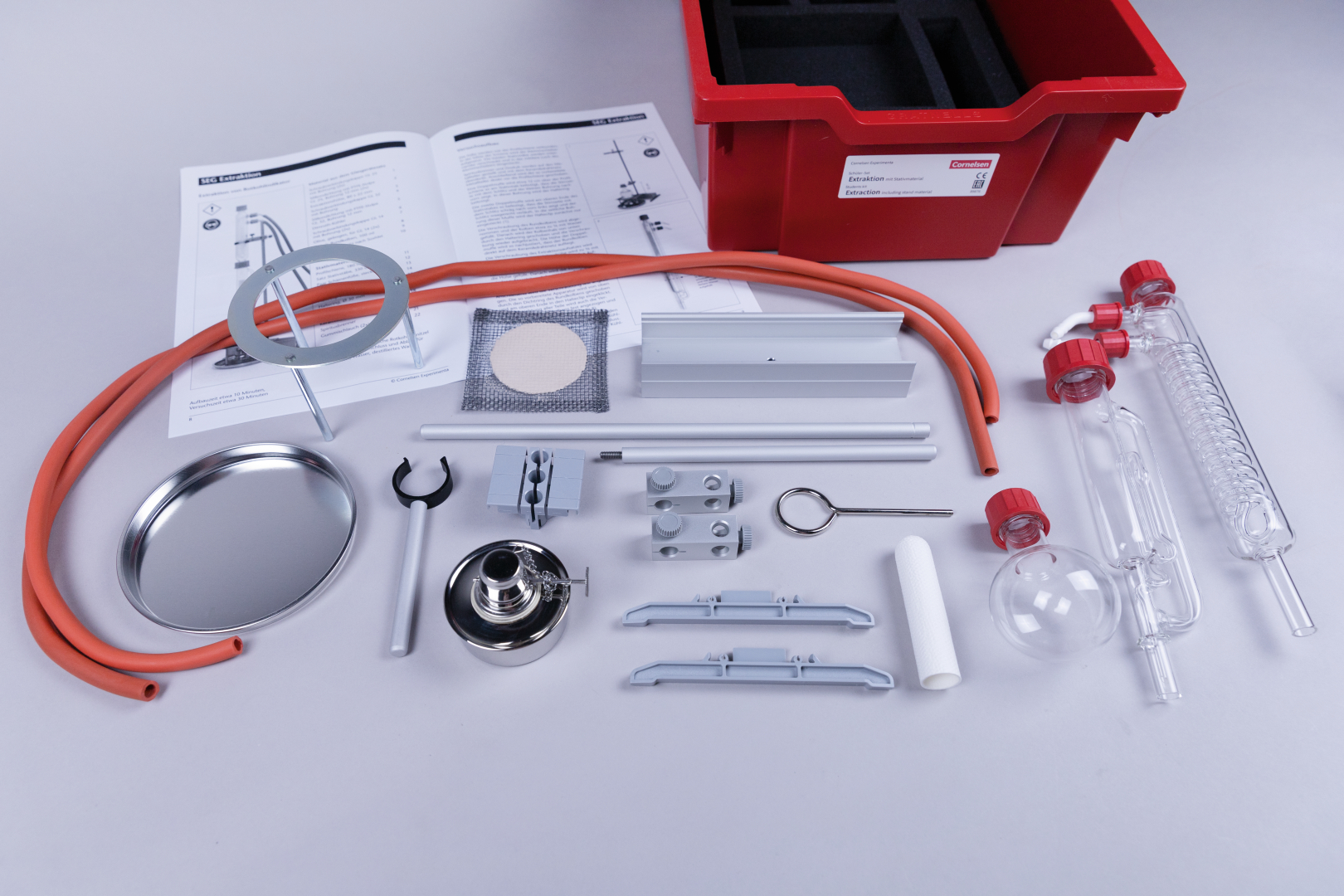 The image shows a selection of experiment materials, including tubes, glass components and a red storage box. In addition, instructions and various tools for educational experiments are shown.