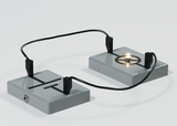 The picture shows two grey boxes connected by wires. A small light bulb is lit in the right box, indicating a simple electrical circuit that can be used for educational experiments.