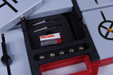 The picture shows an experiment kit with various components, including two measuring probes, a battery and several metal balls, all in a sturdy storage box. The equipment is typical for use in education to carry out physics experiments.