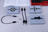 The picture shows various experimental components, including control boxes with different symbols, connecting cables and a light bulb. These materials are designed for educational experiments in the field of electrical engineering and offer hands-on learning opportunities.