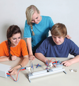 The picture shows three students working on an experimental apparatus equipped with electric motors and propellers. They are concentrating on carrying out the experiment, which is likely to teach physics concepts such as motion and propulsion.