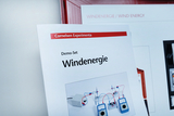 The picture shows instructions for a demo set on wind energy, published by Cornelsen Experimenta. In the background you can see devices and cables that are used to carry out experiments on wind energy use.