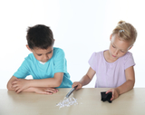 The picture shows two children working at a table. The girl is using a pen to experiment with a piece of black fabric and small scraps of paper while the boy watches attentively.