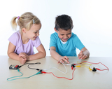 The picture shows two children enthusiastically working on an experiment with electrical components. They connect cables and components to build a circuit and learn the principle of using electrical current in a playful way.