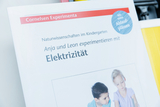 The picture shows a brochure from Cornelsen Experimente, which deals with scientific experiments in kindergarten. The title is about the children Anja and Leon experimenting with electricity.