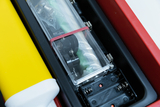 The picture shows an opened experiment kit with various components, including a transparent case with a battery and mechanical parts. Next to it lies a yellow object, presumably part of the kit used for experimental purposes.