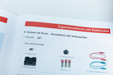 The picture shows a page from a textbook about experiments with electricity. It lists materials that are needed to experiment with an electrical circuit with consumers, such as a light bulb, lamp socket and batteries.