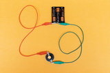 The picture shows an arrangement of two batteries connected to a contact by colored wires. This configuration is probably used for conducting electrical experiments in educational settings.