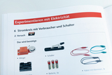 The picture shows instructions for experimenting with electricity, specifically for setting up an electrical circuit with consumers and switches. It lists the materials needed, including a bell, switches, batteries and cables.