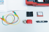 The picture shows various experiment materials, including colored wires, a bell, a battery holder, a switch and batteries. These materials are part of an educational electrical experiment kit.