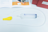 The picture shows a yellow balloon, a transparent syringe with a measuring unit, a hose-shaped connector and instructions. These materials are part of an experiment on the topic of water and air, which is prepared for use in the classroom.