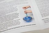 The image shows a person using a hand-held vacuum pump to remove air from a transparent space capsule containing blue contents. Instructions for safe use and cleaning are printed around the capsule.