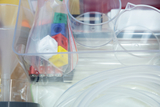 The picture shows a transparent box with various experimental materials, including beakers, batteries and colored building blocks. It also contains pieces of tubing and other equipment for scientific experiments.