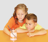The picture shows a girl and a boy staring intently at a glass of water with ice cubes. They are obviously experimenting and observing how a grey straw is placed in the glass.