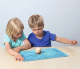 The picture shows two children playing with an experimental device in a concentrated manner. A ball lies in a container on a blue cloth while one of the children pulls on a thread to carry out a physics experiment.