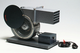 The picture shows an experimental device in the form of a fan with a round lid and a rectangular outlet. The device is operated with a power cable and is suitable for educational purposes in the field of physics or technology.