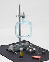 The picture shows various laboratory equipment for experiments, including a holder with a square glass dish, a test tube with yellow liquid, a heater and a book of matches. These materials are arranged on a dark surface and are suitable for educational chemistry experiments.