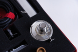 The picture shows a metal apparatus lying in a black foam insert. Surrounded by other materials and tools, it appears to be part of an experiment set for educational purposes.