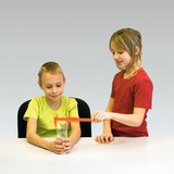 In the picture, two children are conducting an experiment. One child wearing a green t-shirt is measuring the water level in a glass with a red measuring device while the other child is watching attentively.