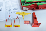 The picture shows an experiment set with various measuring instruments, including two yellow and red holders and a box of measuring balls. There is also a manual open that contains instructions on how to carry out experiments.