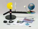 The image shows an experiment kit for illustrating astronomy concepts, including a tellurium with a yellow lamp and a globe. Also shown are instructions, cables, accessories and a marker needed to perform the experiments.
