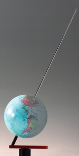 The image shows a colored globe mounted on a sturdy base with a marking on the surface. A long metal pin protrudes from the top of the globe, suggesting a special function or presentation.