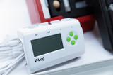 The picture shows a V-Log device connected with several connection cables. It has a display and various buttons for operation, ideal for experiments in the educational field.