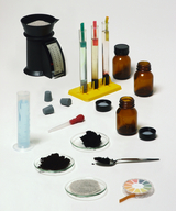 The picture shows a collection of experimental materials, including measuring instruments, test tubes with various liquids, and jars with powder. You can also see pipettes and a color scale for determining pH, which can be used for chemical experiments.