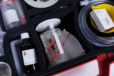 The image shows an experiment kit with various scientific materials, including a bottle of chemical solution, a transparent device, and several containers. The components are neatly arranged in a foam insert to ensure safety and organization.