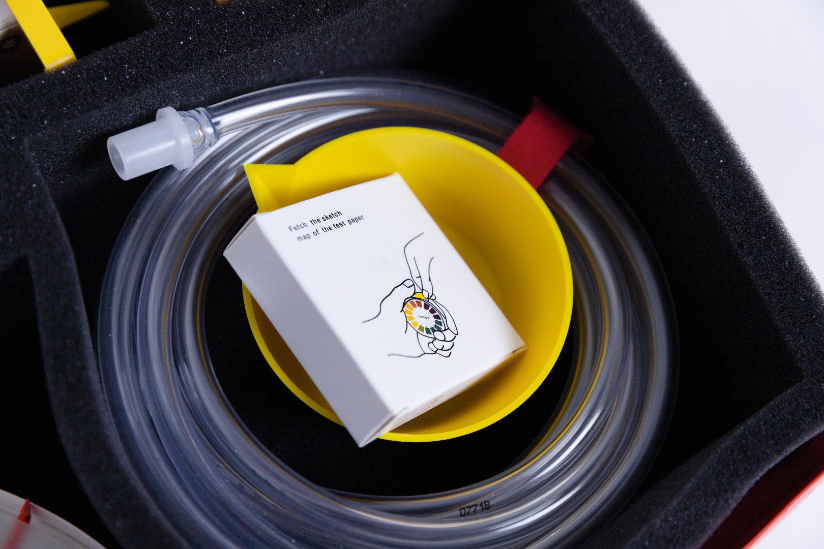 The picture shows an experiment kit that contains a yellow bowl, a tubing system and a small white package with instructions. These materials are designed for educational purposes in German classes and support practical experiments.