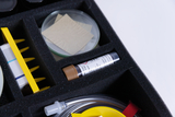 The picture shows a box with various experimental materials, including a Petri dish, cutting patterns and a test tube. These are carefully arranged in a foam insert for safe transport and storage.