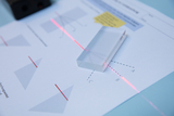 The picture shows a transparent prism lying on a worksheet containing diagrams of the refraction of light rays. Red laser lines illustrate the path of the light through the prism and the corresponding angles at points A, B and C.